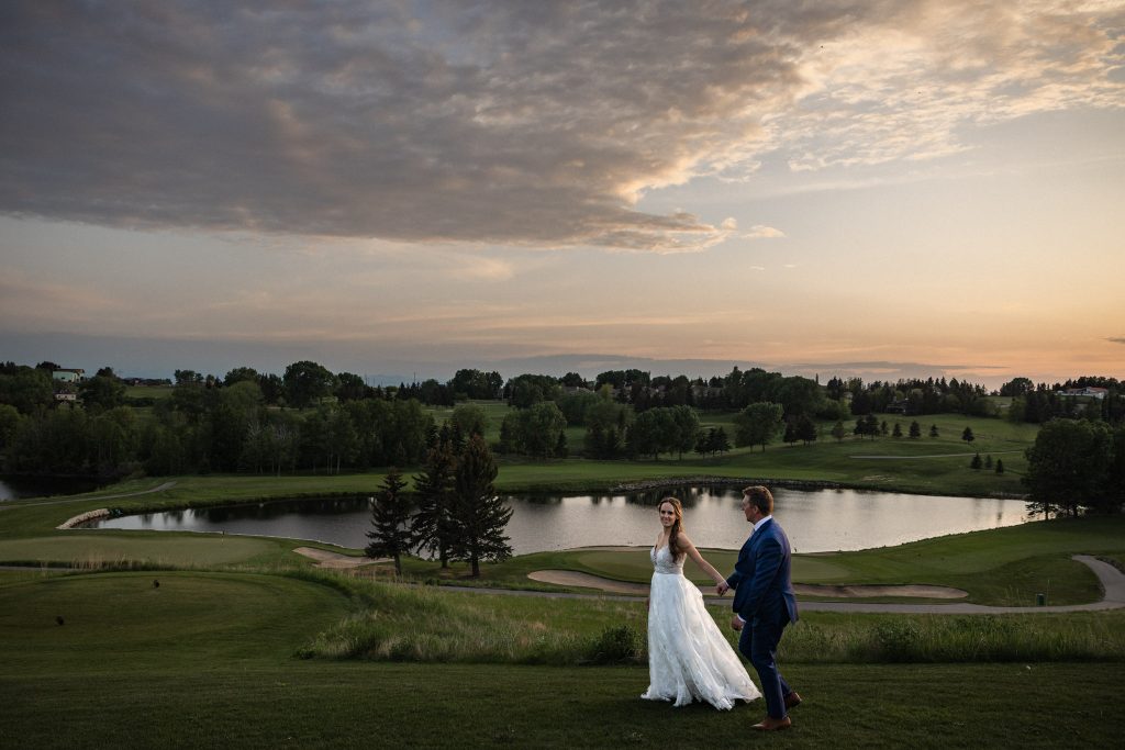 Couple walks along golf course at sunset on wedding day at Bearspaw Golf Course