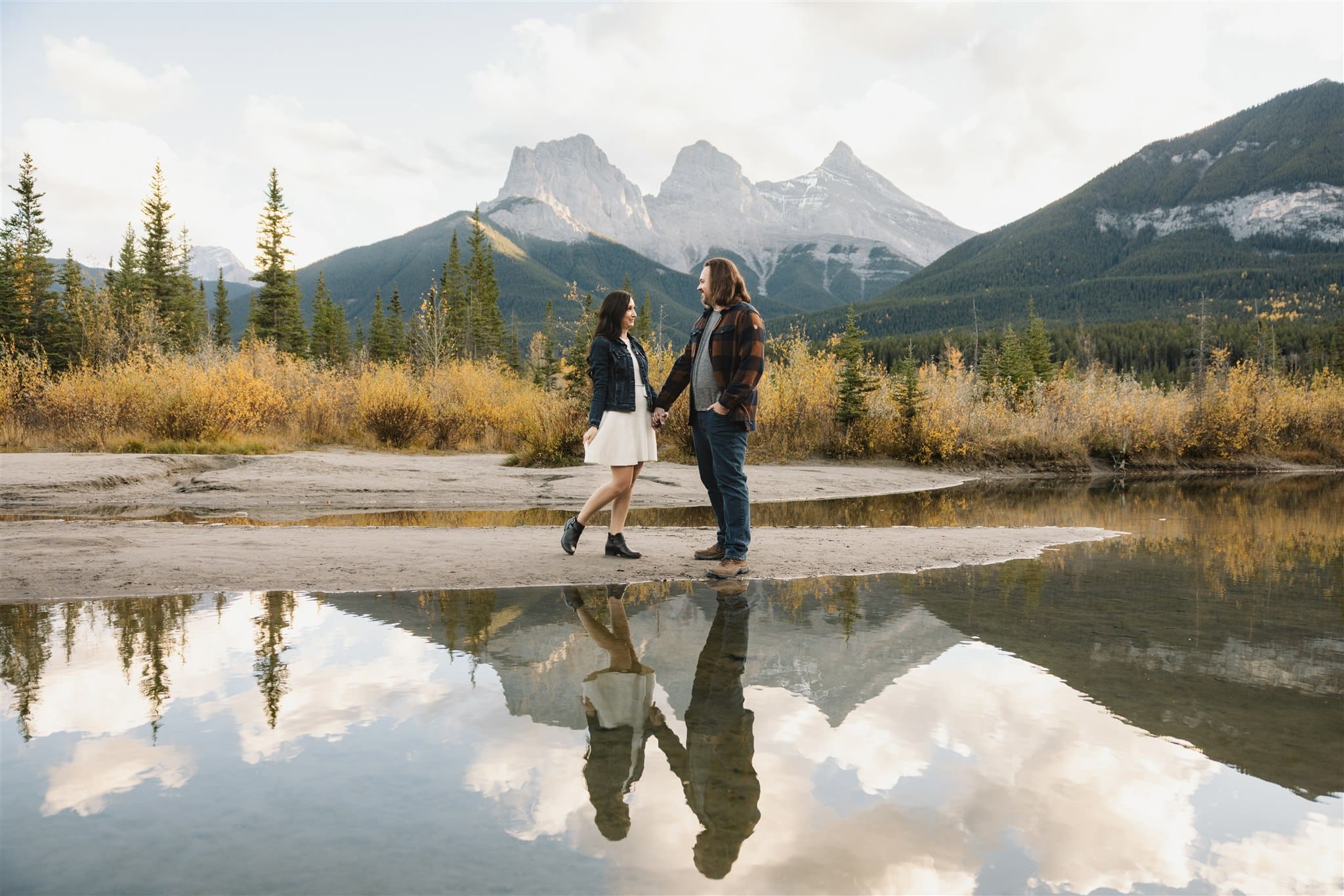 couple takes engagement photos in Canmore with view of Three Sisters Mountain